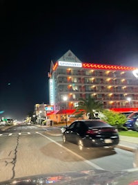 a car driving down the street in front of a hotel at night