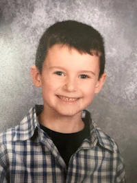 a boy in a plaid shirt is smiling for the camera